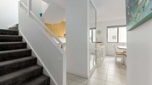 Un interior moderno con una escalera, un comedor y una cocina visibles a través de puertas de vidrio.