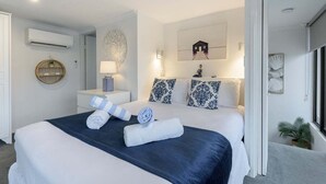 Una habitación de hotel moderna con una cama grande, un espejo redondo, aire acondicionado en la pared y una pequeña planta en maceta.