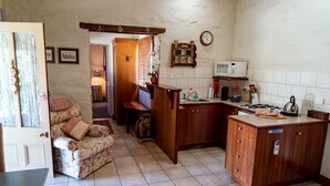 A compact kitchen with wooden cabinets, a microwave, and a gas stove. There is a floral sofa and a wooden rocking horse in the living area.