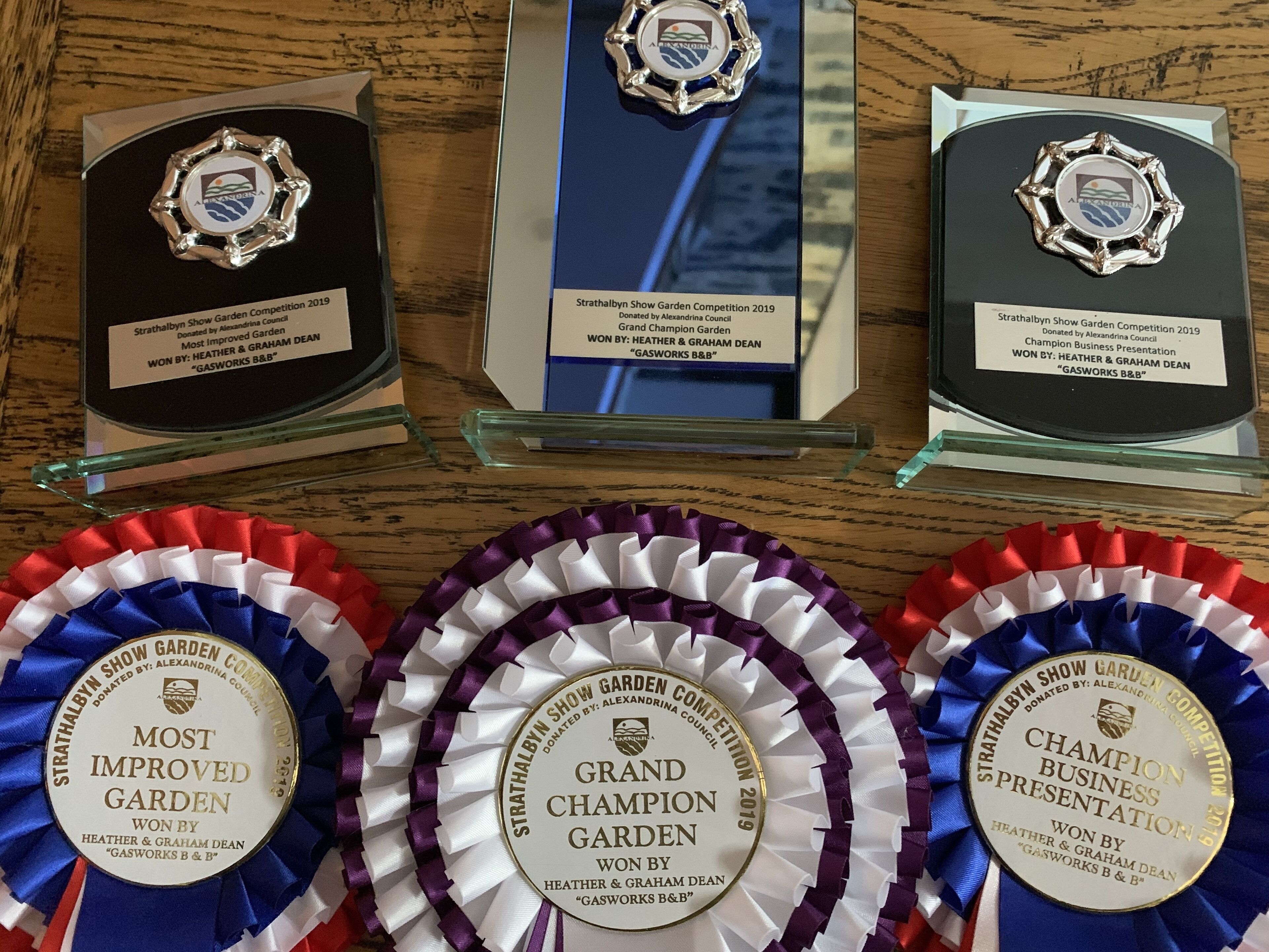 Three awards for the Strathalbyn Show Garden Competition 2019, with ribbons and plaques displayed on a wooden surface.