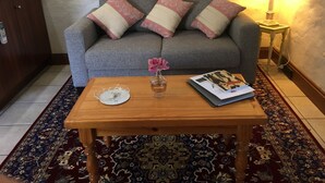A grey sofa with pink and cream pillows, a wooden coffee table with a vase of pink flowers, a book, and a lamp.