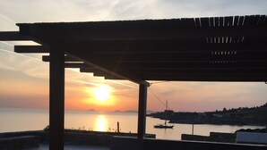 A wooden deck with a pergola overlooking a calm body of water at sunset. - Villa Frear I with infinity pool (KYKLADES)