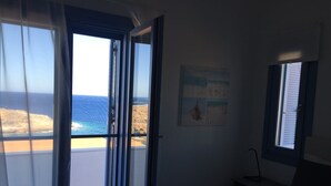 A bedroom with a bed, a nightstand, and a painting. There is a window with a view of the beach. - Villa Frear I with infinity pool (KYKLADES)