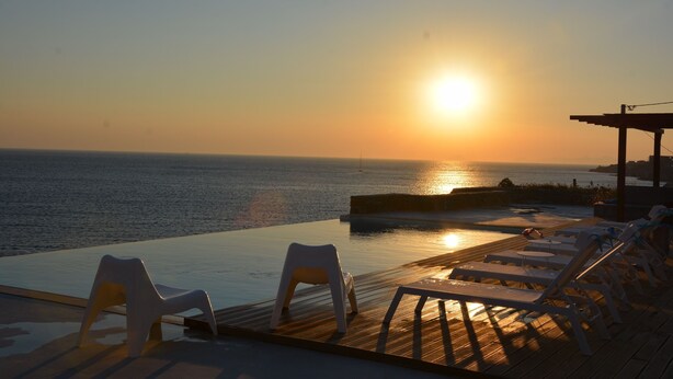 An infinity pool with lounge chairs overlooking the ocean at sunset. - Villa Frear I with infinity pool (KYKLADES)