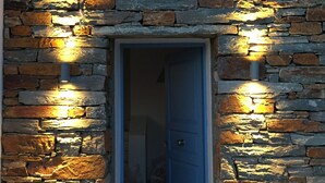 A stone wall entrance with a blue door and two wall-mounted lights. - Villa Frear I with infinity pool (KYKLADES)