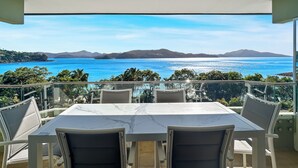 Une terrasse avec une table et des chaises, offrant une vue panoramique sur la mer et les montagnes lointaines.
