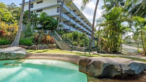 Un hôtel doté d’une piscine, entouré d’une végétation tropicale et comprenant un immeuble à plusieurs étages avec des balcons.