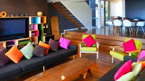 Un salon moderne avec un canapé noir, des coussins colorés, une table basse en bois et un téléviseur.