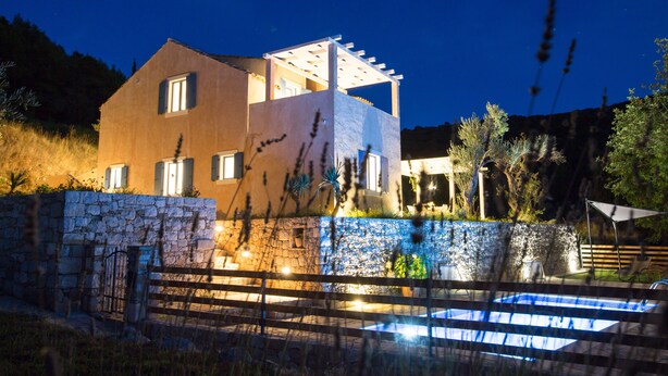 Ein modernes Haus mit Steinwand, Schwimmbad und einer Pergola.