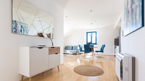 Ein modernes Wohnzimmer mit einem weißen Schrank, einem Essbereich mit blauen Stühlen und einem großen Fenster.