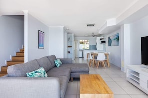 A modern living room with a grey sectional sofa, a wooden coffee table, and a TV stand.