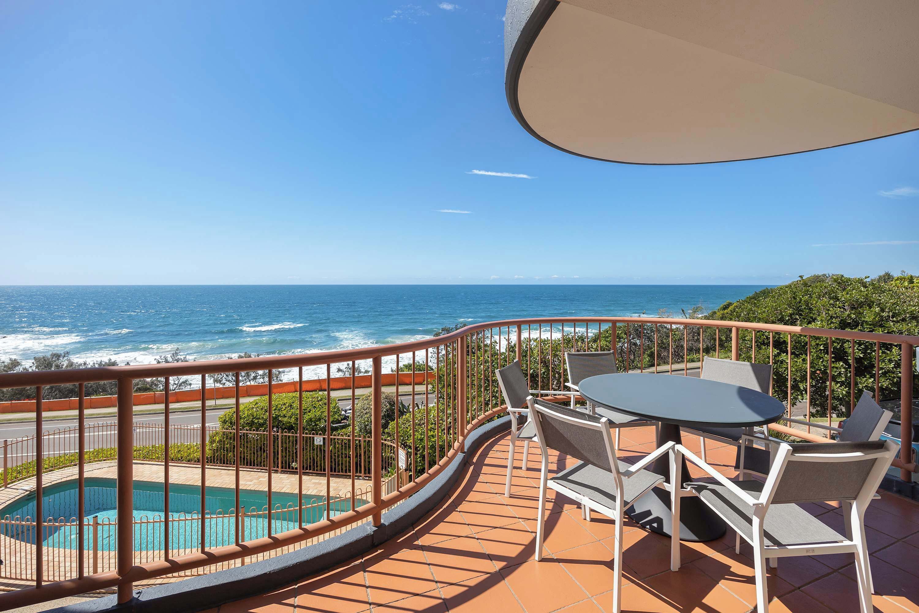 A balcony with a pool, outdoor seating, and a view of the ocean.
