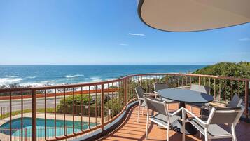 A balcony with a pool, outdoor seating, and a view of the ocean.