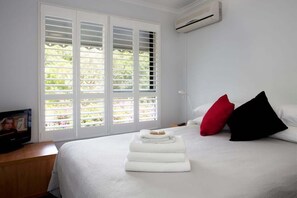 Et hotelværelse med en seng, hvide gardiner, et klimaanlæg og et vindue med rullegardiner.