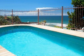 A swimming pool with a curved edge, a metal fence, and a view of the ocean.