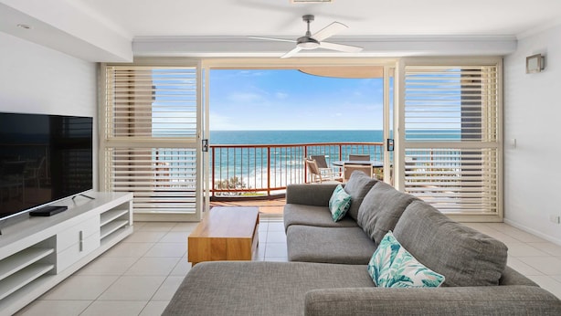 Un salon doté d’une grande télévision, d’un canapé, d’une table basse et d’un balcon offrant une vue sur la plage.