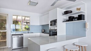 Une cuisine moderne avec des meubles blancs, un îlot central doté de tabourets, un lave-vaisselle et un four à micro-ondes encastré.