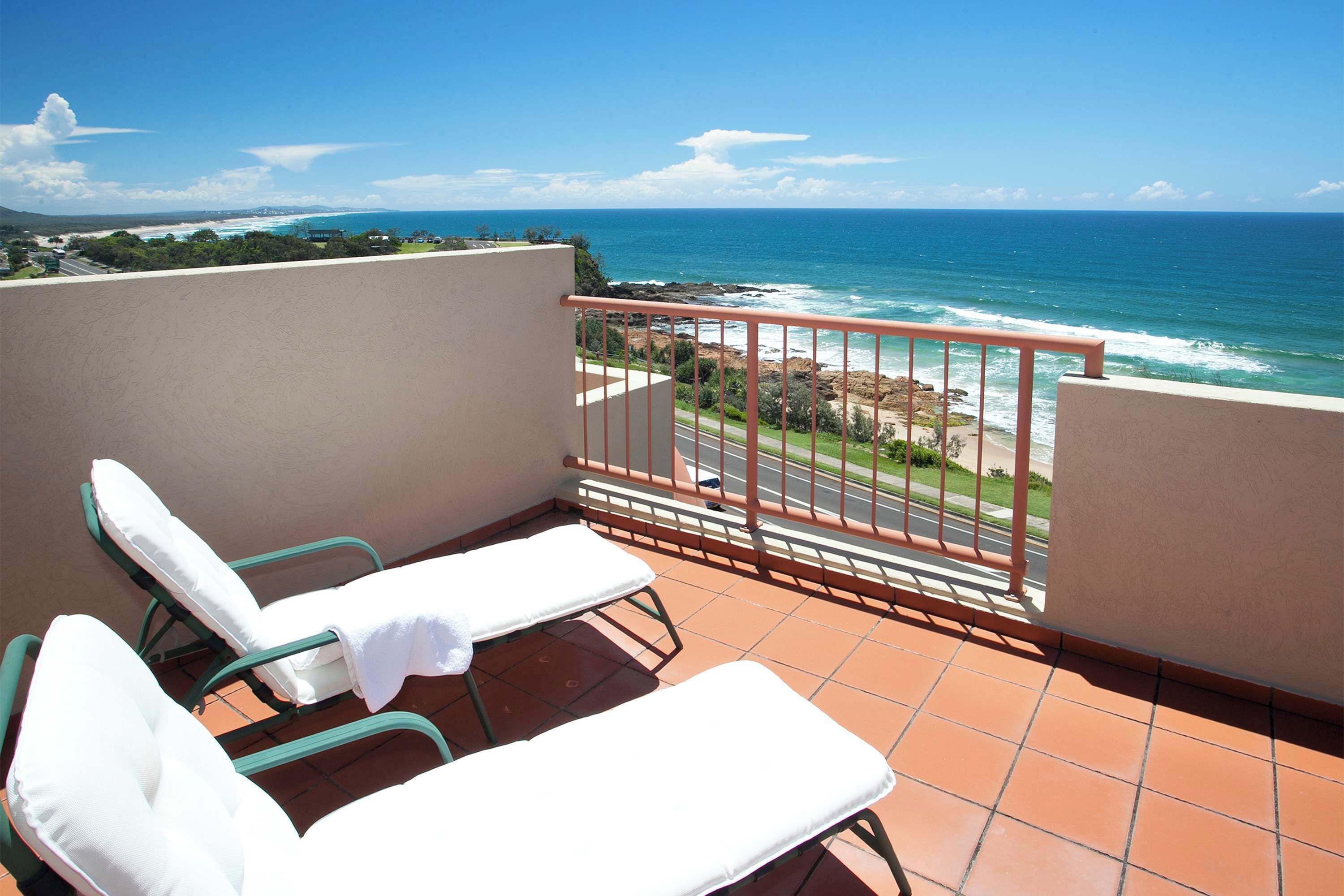 Un balcon avec deux fauteuils de relaxation blancs dotés de coussins, une rambarde rouge et une vue sur l’océan.