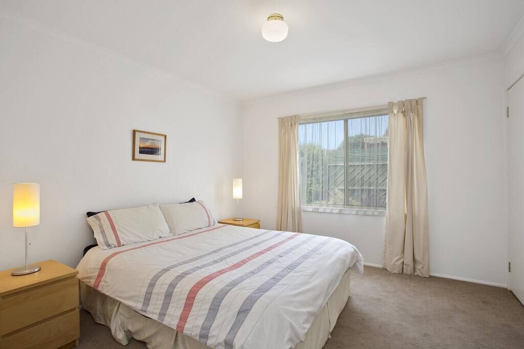 A bedroom with a bed, bedside lamps, a window with curtains, and a small picture on the wall.