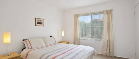 A bedroom with a bed, bedside lamps, a window with curtains, and a small picture on the wall.