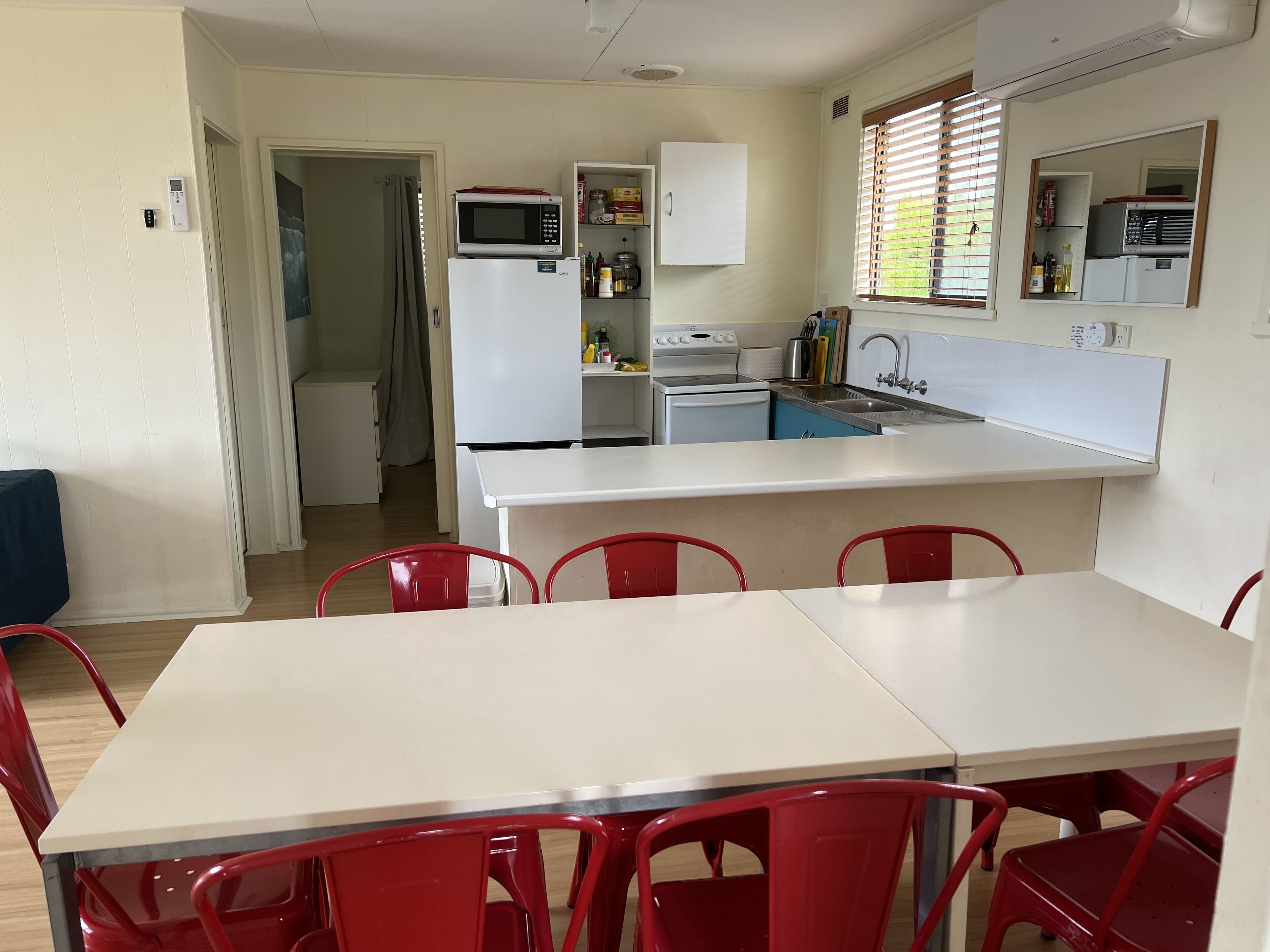 A compact kitchen with a refrigerator, microwave, stove, and sink. There is a dining table with red chairs.