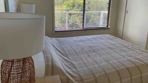 Ein Schlafzimmer mit einem Bett, einem Fenster mit Jalousien und einer Lampe.