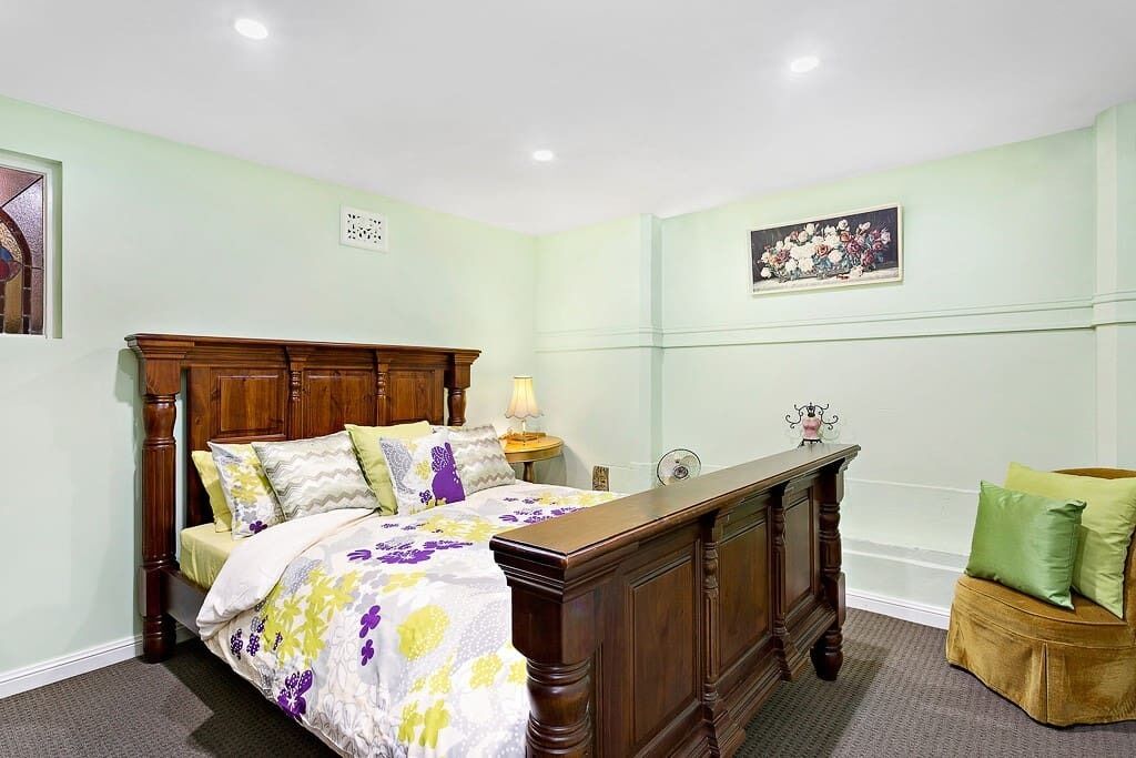 A bedroom with a wooden bed, a nightstand, a green armchair, and a painting on the wall.