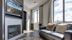 A modern living room with a fireplace, a leather sofa, and large windows offering a city view. - Perfect Located 2-Bed Blue Mountains Getaway (Katoomba)