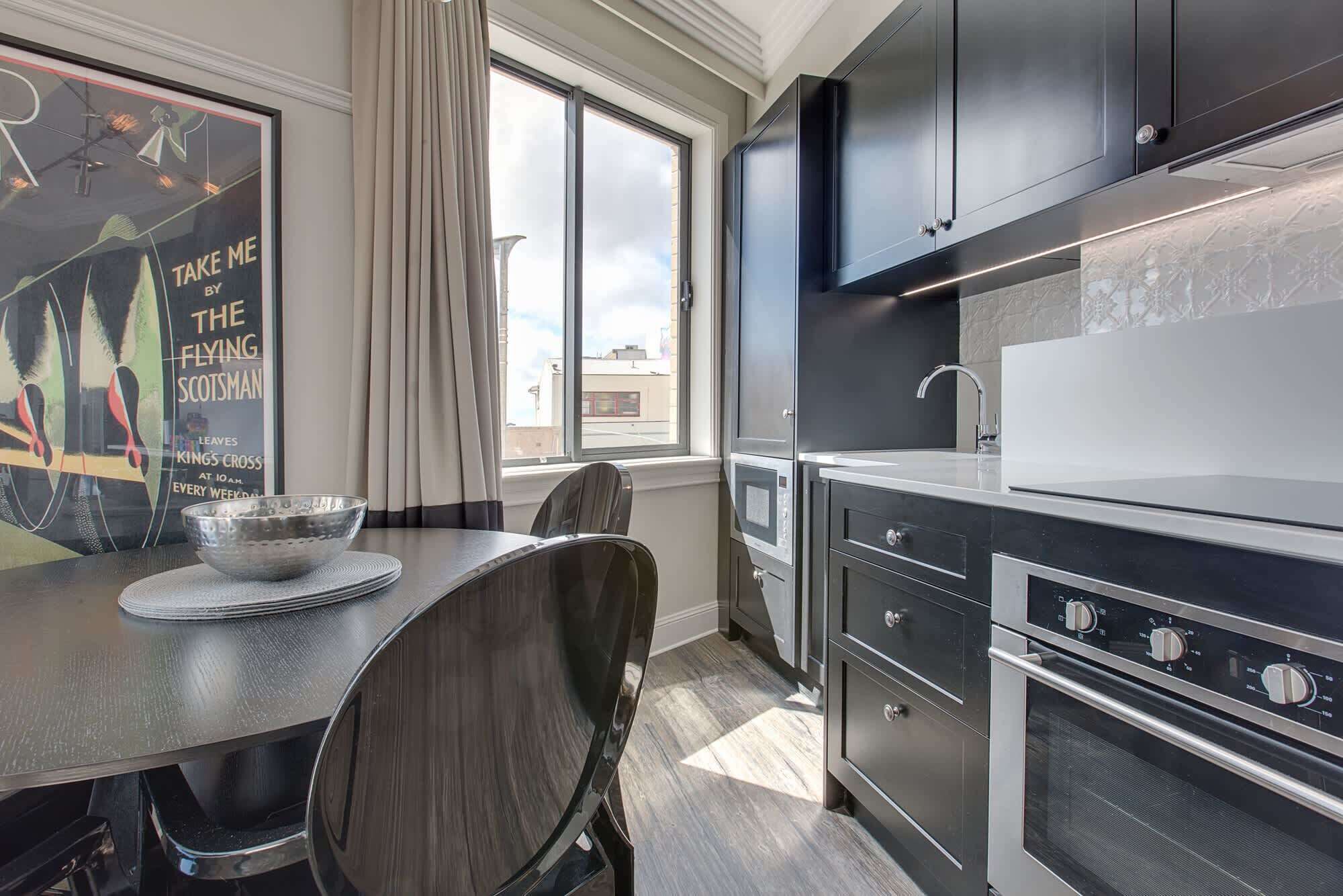 A modern kitchen with stainless steel appliances, a dining table with a bowl, and a poster on the wall.
