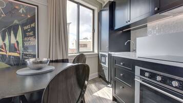A modern kitchen with stainless steel appliances, a dining table with a bowl, and a poster on the wall.
