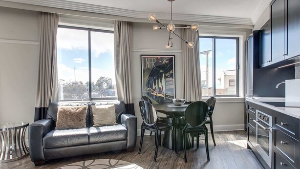 A modern living room with a sofa, dining table, chairs, and a kitchen area with cabinets and a TV. - Perfect Located 2-Bed Blue Mountains Getaway (Katoomba)