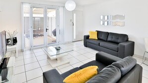Een moderne woonkamer met een zwarte leren bank, een glazen salontafel en een geel kussen.