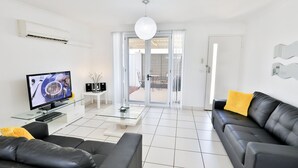 Een moderne woonkamer met een flatscreen televisie, zwarte leren banken, een glazen salontafel en een schuifpui naar een buitenruimte.