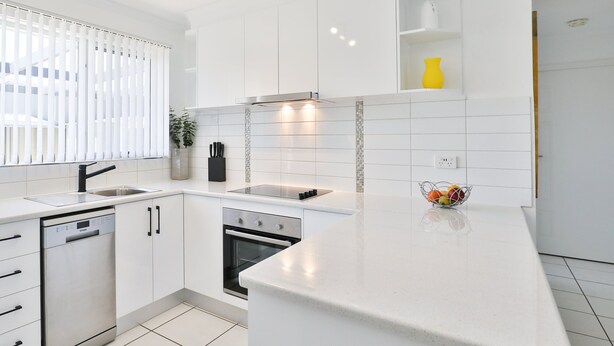 Een moderne keuken met witte kastjes, een ingebouwde oven en een groot kookeiland met een spoelbak.