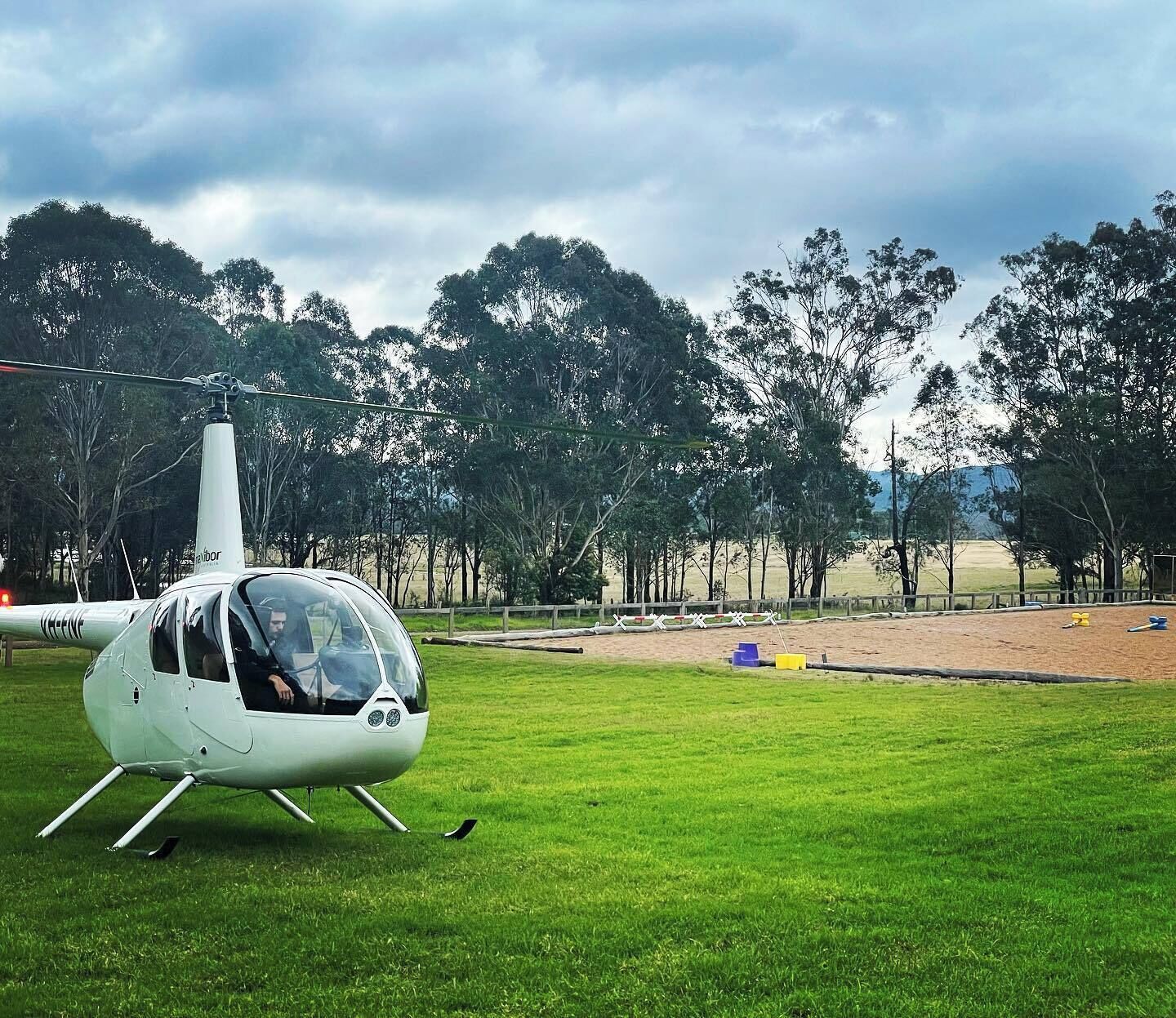 Un helicóptero sobre un campo cubierto de hierba, con árboles al fondo.