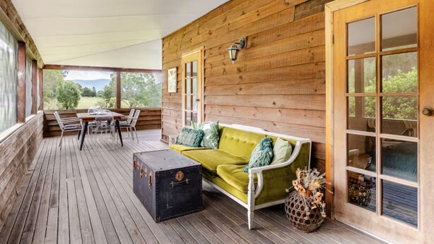 A wooden deck with a sofa, table, and chairs, a suitcase, and a decorative vase. - Newly Renovated with aircon throughout! Family, Horse and Dog Friendly Getaway (Congewai)
