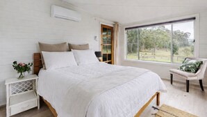 A bedroom with a large bed, a nightstand, a chair, and a window with a view of greenery. - Newly Renovated with aircon throughout! Family, Horse and Dog Friendly Getaway (Congewai)