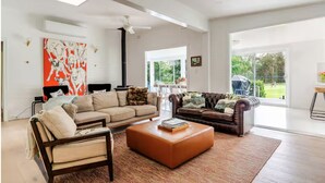 A spacious living room with a large window, a fireplace, and a modern ceiling fan. - Newly Renovated with aircon throughout! Family, Horse and Dog Friendly Getaway (Congewai)