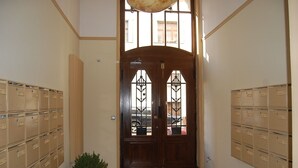 Un pasillo con una puerta doble de madera, paredes color beige y una planta en maceta. Casilleros de correo a lo largo de ambos lados del pasillo.