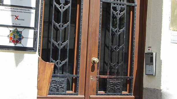 Puerta doble de madera con rejas metálicas y pomo de latón.