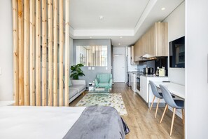 Un espacio habitable moderno y funcional con kitchenette, comedor y zona de estar con sofá y sillones.