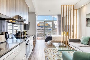 Un apartamento moderno con cocina, comedor, sala de estar con sofá y mesa de centro, y un amplio ventanal con vistas a la ciudad.
