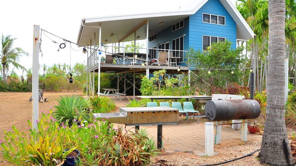 A blue house with a covered patio area, outdoor seating, and a barbecue grill.