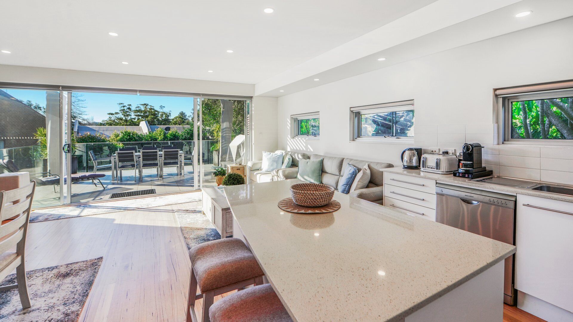 A modern kitchen with a large island, a dining area with a wooden table and chairs, and a view of the backyard through glass doors.