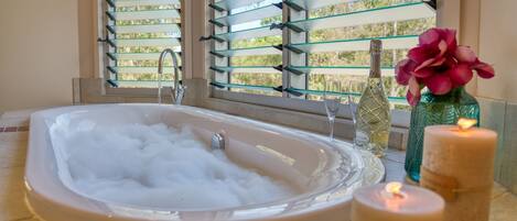 Un baño con una bañera llena de burbujas, una ventana con persianas y velas.