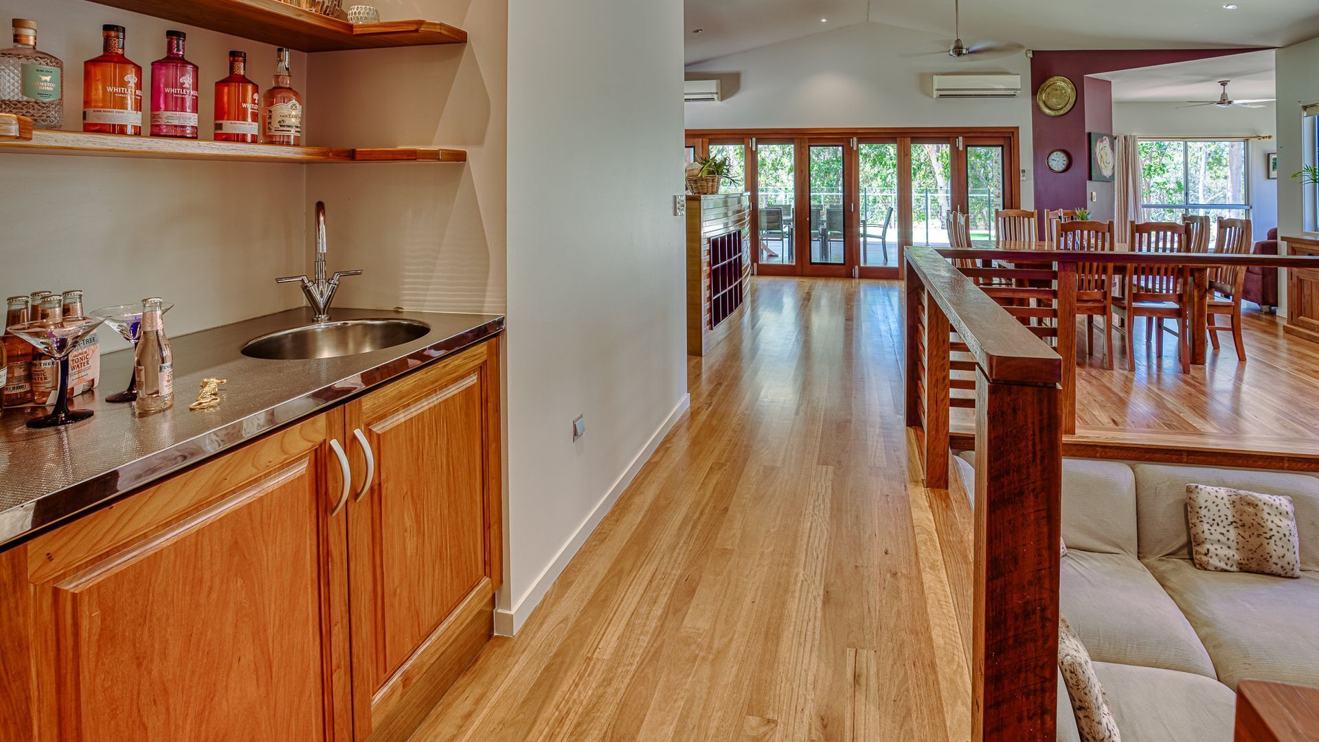 A spacious kitchen with wooden cabinets, a stainless steel sink, and a variety of bottles on the countertop.
