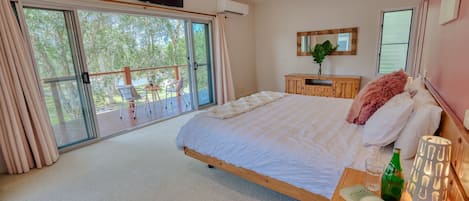 Un dormitorio con una cama grande, una mesita de noche de madera, un televisor y una puerta corrediza de vidrio que da a un área exterior con sillas.