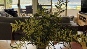 A room with a large window overlooking mountains and a lake, a wooden table with a vase of flowers, and a sofa with cushions.