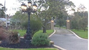 Une allée privée fermée par un portail, agrémentée d’un lampadaire et d’une statue.