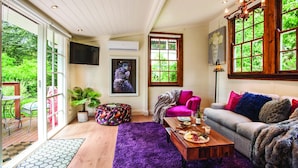 Un salon chaleureux avec un canapé, une table basse et une table à manger dressée avec de la nourriture et des boissons. Une grande fenêtre offre une vue sur la verdure environnante.